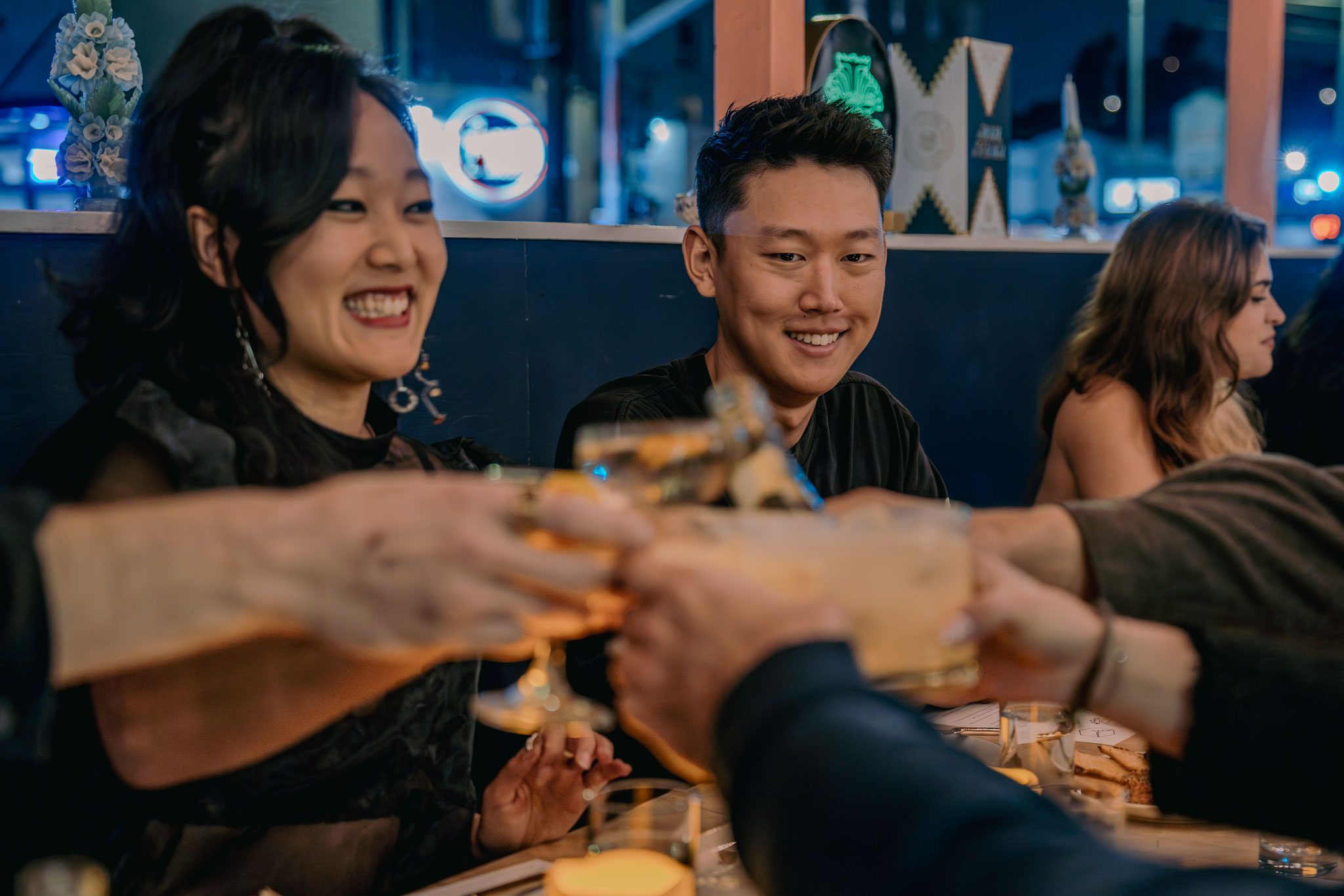 Group of people clinking glasses together at a dimly-lit restaurant, smiling and enjoying their time.